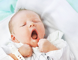 A yawning newborn baby with a hospital ID bracelet.