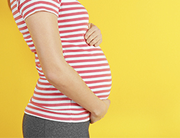 The belly of a pregnant woman in a striped shirt.